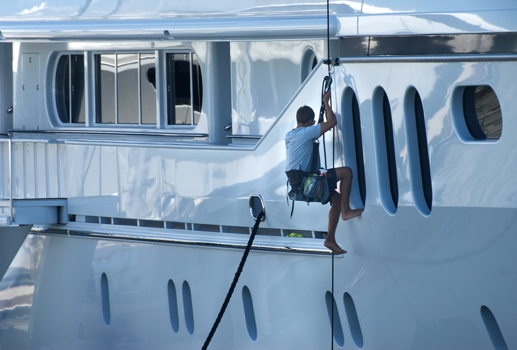 Detail technician working on the white hull of a large motor yacht